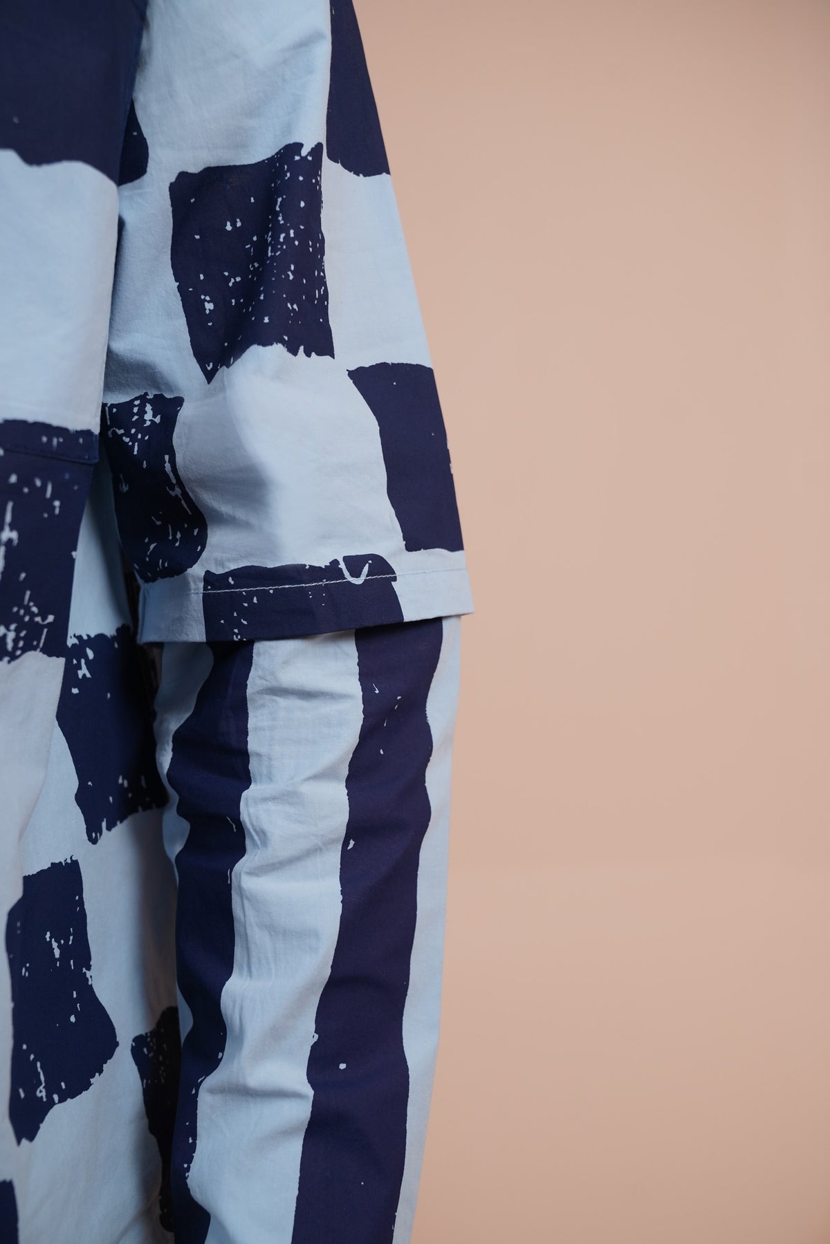 Close-up of a garment with a navy and light blue abstract block pattern, shown against a solid peach background.