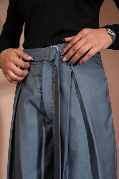 Close-up of a person wearing high-waisted slate blue pleated trousers with a matching belt and silver buckle, paired with a black long-sleeve top.