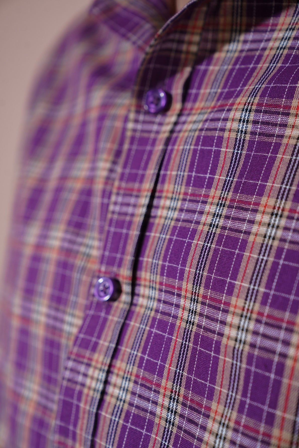Close-up of a purple plaid button-up shirt with matching purple buttons, showing the fabric pattern and collar detail.