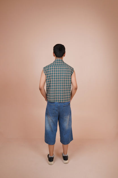 A man viewed from behind wearing a sleeveless shirt and blue denim shorts, standing against a solid peach-colored studio background.