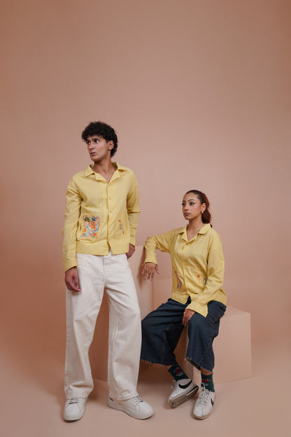 A man and a woman modeling matching pale Yellow long sleeve button up shirt with colorful embroidered details on the front, posed against a solid dusty pink studio backdrop.